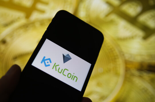 Viersen, Germany - February 9. 2021: Closeup of mobile phone screen with logo of kucoin lettering trading platform, blurred bitcoins background