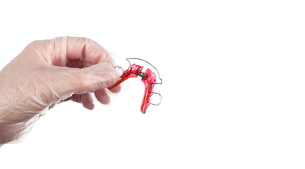 An orthodontist hand wearing disposable gloves shows an orthodontic appliance for children on white background with copy space