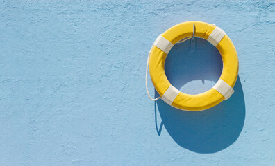 Yellow circular lifebuoy hanging on blue wall with copy space