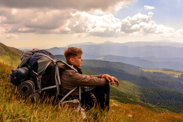 Fototapeta na wymiar A young tourist sits on a background of mountains with a backpack, relaxing and admiring the views of the Carpathians in Ukraine.