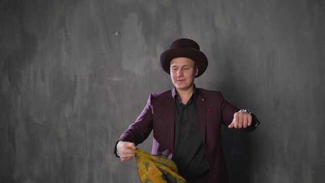 Illusionist is doing magic trick in slow motion. Magician man in black suit is showing trick doing metal stick from headscarf and looking at camera. Concept of performances, shows and circus. Magician