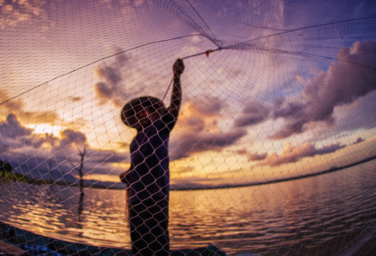 fisherman casting a net into the water during at sunrise