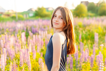 Naklejka na ściany i meble Happy teenage girl smiling outdoor. Beautiful young teen woman resting on summer field with blooming wild flowers green background. Free happy kid teenager girl childhood concept
