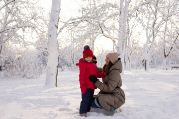 Fototapeta na wymiar Happy mom and daughter 6 years old in a winter park are playing in the snow. Family and childhood concept. Holidays and children's parties.