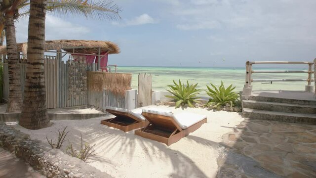 Smooth tracking shot of sun loungers in idyllic perfect setting under palm trees overlooking the sea on tropical island
