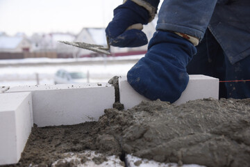 The bricklayer puts bricks in cement in straight rows, makes a concrete wall.