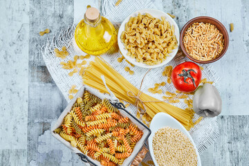 Bowls of uncooked pasta, spaghetti, a basket of fusilli, vegetables