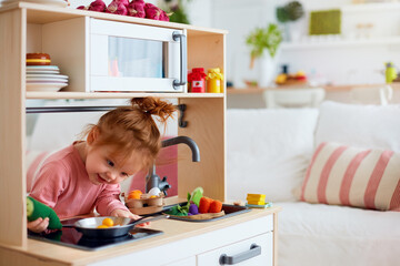 funny toddler baby girl playing on toy kitchen at home