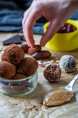 Healthy energy protein balls with dates, oats, peanut butter and dark chocolate. Homemade gluten free truffle bites covered with cocoa powder or almonds. Vegan raw appetizer. Hand in background.