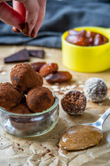 Hand sprinkles cocoa powder on healthy energy protein balls with dates, oats, peanut butter and dark chocolate. Homemade gluten free truffle bites with no bake. Vegan raw appetizer or snack. Side view