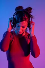 Zelfklevend Fotobehang Attractive woman with headphones listening music in studio with blue and red lights © Bisual Photo