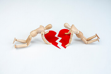 two wooden mannequins trying to mend up a red broken heart