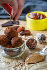 Hand sprinkles cocoa powder on healthy energy protein balls with dates, oats, peanut butter and dark chocolate. Homemade gluten free truffle bites with no bake. Vegan raw appetizer or snack. Side view