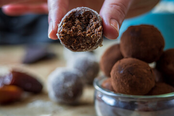 Close up on half eaten healthy energy protein ball with dates, oats, peanut butter and dark chocolate. Homemade gluten free truffle bites covered with cocoa powder or almonds. Vegan appetizer or treat