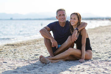 Coppia innamorata si abbraccia affettuosamente seduti nella sabbia di una spiaggia al mare