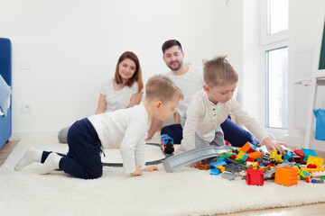 Young family, mom and dad with two young sons, playing with toys in the nursery, happy family having fun together
