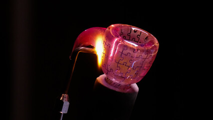 A Lampworker welds a handle to a puzzle patterned bowl made from borosilicate glass 