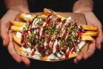 Close view of the hands of a young girl holding a portion gourmet french fries with white and red sauces (mayonnaise and ketchup)