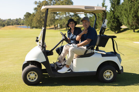 Caucasian senior man and woman driving golf buggy on golf course smiling