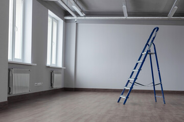 A dirty blue metal stepladder against a newly painted gray wall, windows in a new building. Home Improvement. The concept of professional renovation. Copy space.