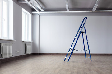 A dirty blue metal stepladder against a newly painted gray wall, windows in a new building. Home Improvement. The concept of professional renovation. Copy space.