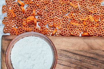 A bowl of flour and scattered heart-shaped pasta on the marble table