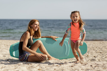 Fototapeta na wymiar Madre in costume da bagno insieme alla figlia si divertono in una spiaggia al mare.