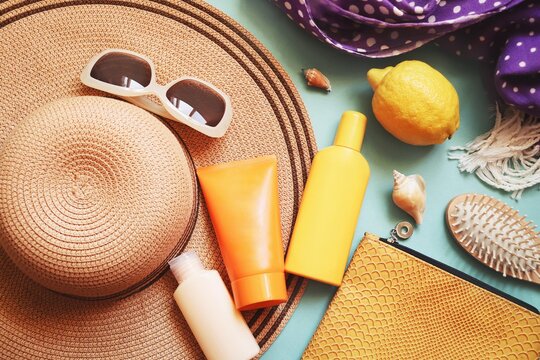 Summer beach essentials flat lay photography. Sunscreen for sensitive skin, moisturizer for face, travel size shampoo, wooden hair brush, straw hat, sunglasses and cosmetic bag