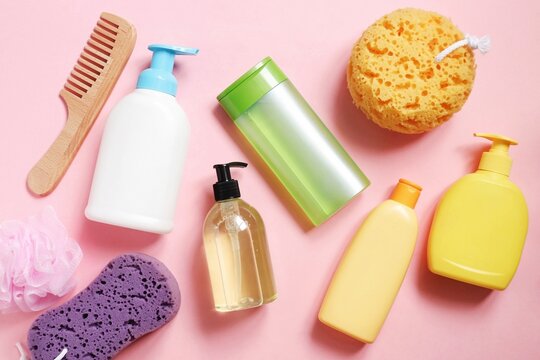 Toiletries and hygiene products. Wooden comb, shampoo, shower gel, hair conditioner, balm and sponges on a pink background. Flat lay beauty photography