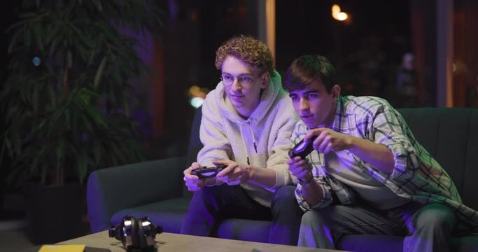Caucasian couple of young adults playing online video game console with joystick gamepads rejoicing funny leisure activity at home.