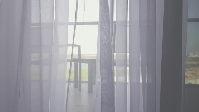 Light breezy sheer curtain blowing in the wind looking towards the balcony behind it, chairs and table