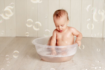 the baby bathes or washes in a basin with foam and soap bubbles