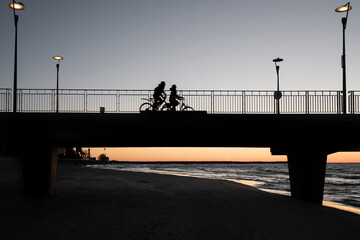 Sylwetka pary rowerzystów na molo w Kołobrzegu o zachodzie słońca - obrazy, fototapety, plakaty
