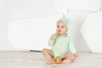 baby eats fruit puree with a spoon in a green bodysuit, feeding and baby food concept