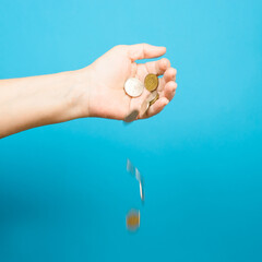 Elderly woman's hand and falling coins, blue background. Selective focus, motion blur. Income loss, poverty concept