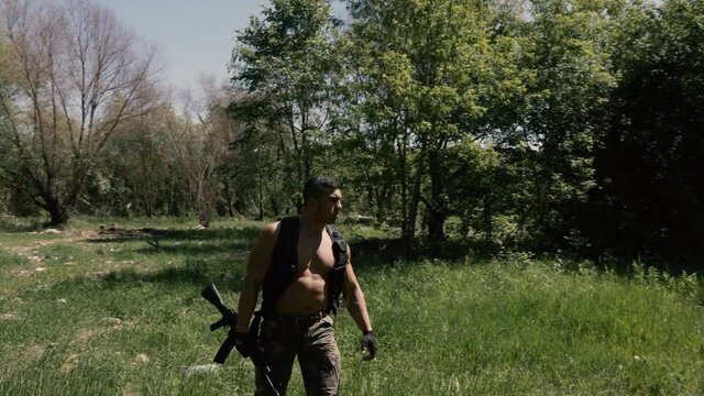 Armed muscular hunk in a military uniform walks through a ruined deserted territory and looks suspiciously around