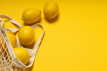 Eco-friendly bag with ripe yellow lemons on yellow background