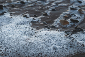 Blyth beach,  the water foam wave, wet sand and small stones. Winter cold day at the beach. Low perspective. Close up view.
Blyth, Northumberland, UK.