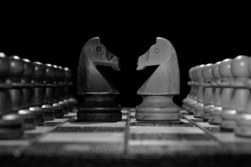 Black and white chess faceoff of both knights horses on top of a chess board in front of a dark...