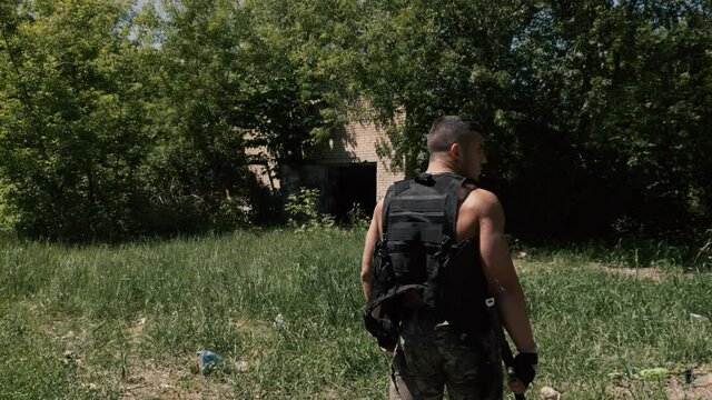 Strong shirtless security guard with strong torso patrolling the territory with a Kalashnikov assault rifle in his hands