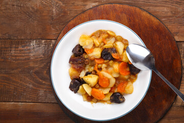 A dish of Jewish cuisine tsimes with carrots and dates in a white plate on a round stand next to a spoon.