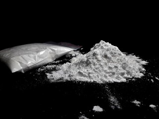 Cocaine drug powder pile and bag on black background
