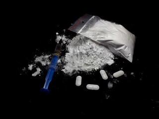 Injection syringe on the cocaine drug powder pile and bag and pills on black background