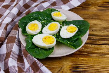 Boiled eggs with fresh spinach leaves and sesame seeds on wooden table
