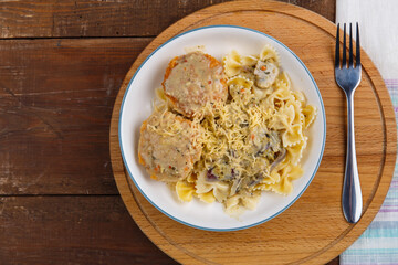 Pasta in a creamy sauce with mushrooms and chicken meatballs in a beige plate on a wooden table on a round stand with a fork