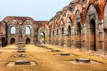The ruins of a broken hall with stone arches at the ancient Baro Shona Masjid in the village of Gour.