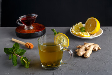 immune ginger drink with honey mint and lemon in a glass cup near ingredients on a concrete background.