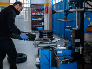 MECHANIC IN HIS WORKSHOP FIXING CAR WHEEL IN MACHINE