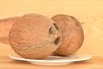 Two ripe organic coconuts on a white plate, close-up, on a natural wood background.