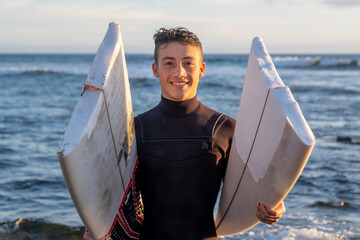 Young surfer comes out of the water carrying the broken board in the middle. Handsome guy with...
